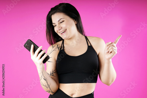 A cheerful athletic young woman looks at her smartphone and is amazed  studio with pink background