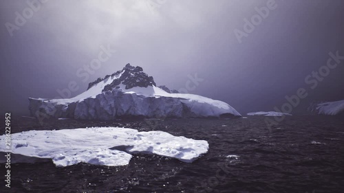 Antarctic iceberg and dark ocean, muted dawn light over jagged peak and frozen foreground, lonely atmosphere with distant swell research vessel beacon imagined