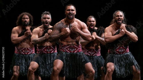 Maori warriors performing a haka dance with fierce expressions and traditional attire against a dark background