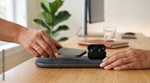Person placing smartphone on a modern wireless charging pad at a desk in a clean home office environment