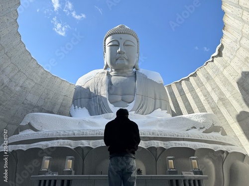 Obraz na plátně Tourist looking at the giant stone Buddha statue covered in snow at the Hill of the Buddha in Sapporo, Japan