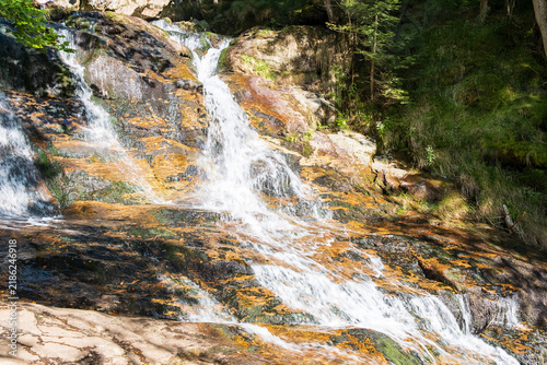 Quadro su tela Mountain waterfall flowing over colorful rocky slope in forest
