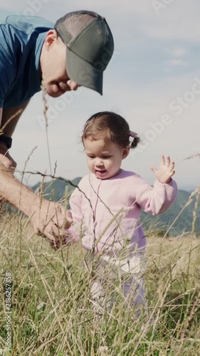 Toddler girl picking flowers with her father in a mountain meadow
