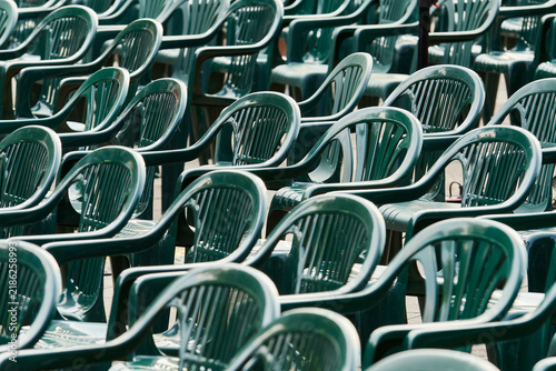 Rows of empty green plastic chairs arranged for a public event or community gathering, creating a visual concept of participation, belonging, social connection, audience and collective activities.