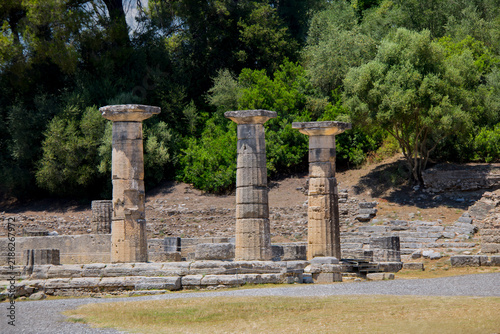 Foto The image captures the sunlit archaeological ruins of Olympia, featuring ancient