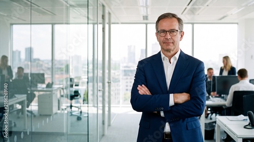 Businessman with glasses and arms crossed standing in a modern office with windows