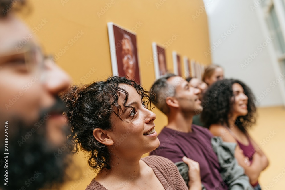 Obraz premium Diverse group of young adults admiring paintings in a bright art gallery, featuring open expressions for cultural and leisure campaigns
