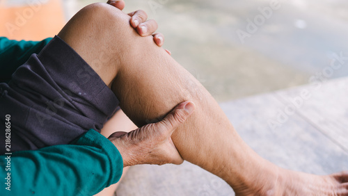Detailed close-up of an elderly adult pressing their aching calf muscle outdoors. The senior is experiencing severe leg pain, poor blood circulation, and physical strain. Aging wellness concept.