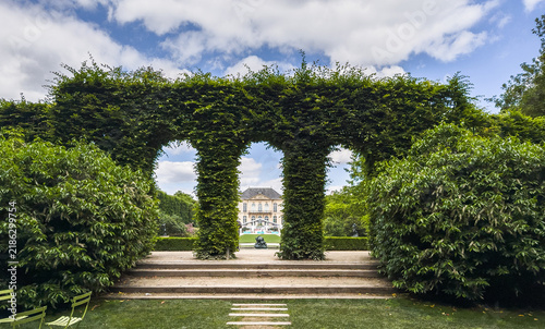 Verdant arches frame a glimpse of the elegant Musee Rodin, blending manicured nature with classic French architecture in Paris.
