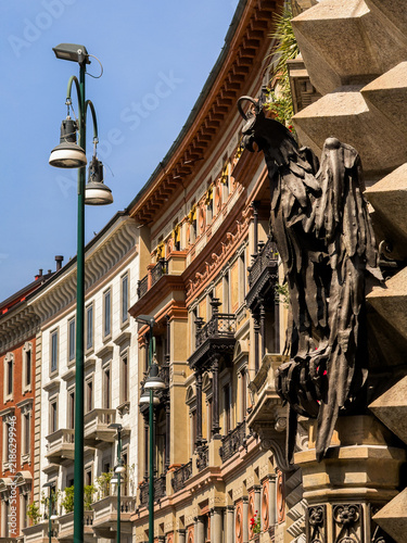 Ornate Italian facades curve beneath a bronze chimera perched against textured stone, blending classic architecture with striking sculptural detail in Milan Italy.