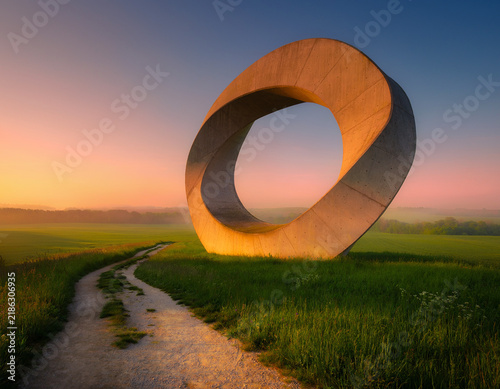 Concrete mobius strip sculpture in green field at sunrise