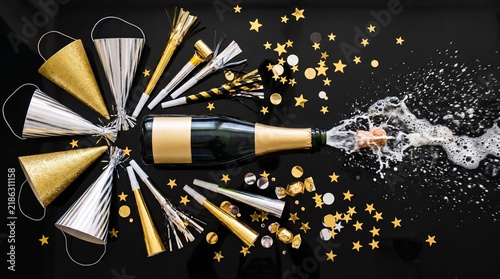 Popping Champagne Bottle with Party Hats Blowers and Gold Confetti on Black Background