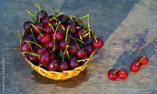 Cuadro en lienzo Fresh sweet cherries in a wicker basket on a wooden table with sun shadows