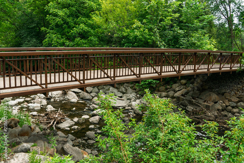 Edward Gardens, Toronto, Canada - A rustic wooden pedestrian bridge crossing a rocky creek surrounded by lush green woodland