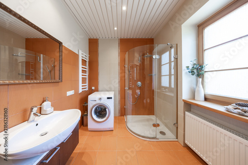 Modern Orange Tiled Bathroom With Curved Glass Shower and Front-Load Washing Machine