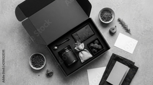Open black gift box containing curated luxury products on a textured surface