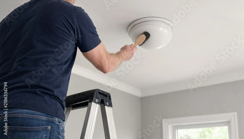 Man standing on a ladder dusting a ceiling light fixture in a renovated apartment room with cleaning lamp home maintenance dusting service domestic chores home improvement cleaning task