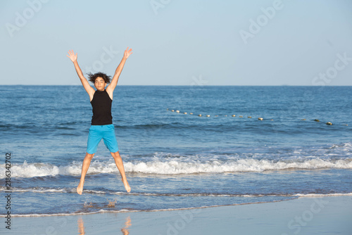 фотографія Happy teenager jumping mid-air on a sunny ocean beach with arms raised in joy