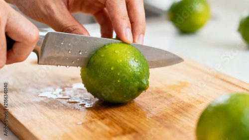  Hands slicing a fresh juicy lime on wooden board
