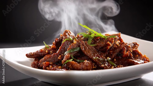 Sizzling beef strips with sauce arranged in a minimalist dish steam effect rich tones light background sharp focus high clarity