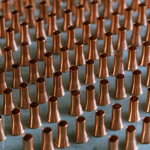 Rows of copper tubes with flared openings on a textured surface