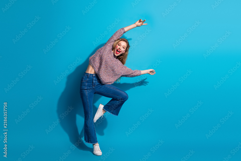 Fototapeta premium Young chic woman jumps in casual sweater jeans against blue background joy energy fashion lifestyle beauty advertising shopping campaigns