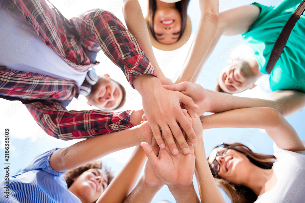 Obraz premium Young friends stacking hands in a circle showing teamwork, unity and friendship during an outdoor summer gathering and celebration