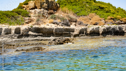 A serene coastal landscape featuring rocky formations and vibrant greenery by the clear blue water.