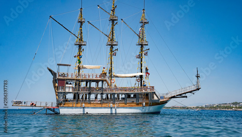 A majestic vintage pirate ship anchored in clear blue waters under a vibrant sky.