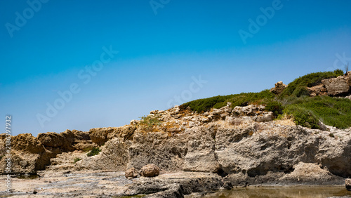 A stunning view of rocky coastline under a clear blue sky, showcasing nature's beauty and serenity.