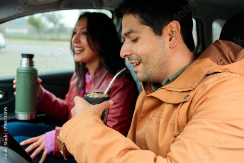 Cheerful Latin friends sharing yerba mate inside car during travel stop