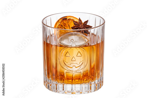 Jack-o'-lantern spiced old fashioned whiskey cocktail with carved pumpkin ice sphere, roasted orange slice, and star anise in crystal rocks glass