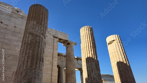 Propylaea, Acropolis of Athens, Greece - 26 June 2026. Weathered fluted columns rise beside the marble wall of the Propylaea beneath a clear blue sky.