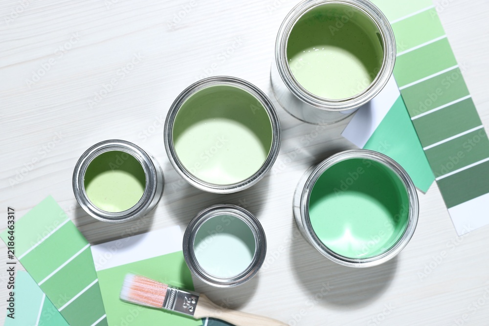 Obraz premium Metal cans with paint in shades of green, brush and color palettes on white wooden table, flat lay