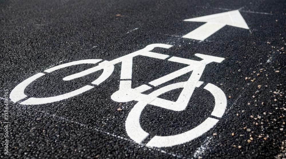 Obraz premium Bicycle lane symbol painted in white on dark asphalt road pavement
