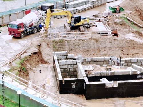 Construction Site With Excavator And Cement Truck Building Foundation In Muddy Urban Work Zone.