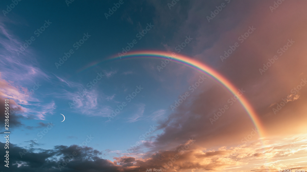 Fototapeta premium A vibrant rainbow arches across a dramatic evening sky with a crescent moon. Ideal for weather and nature background concepts.