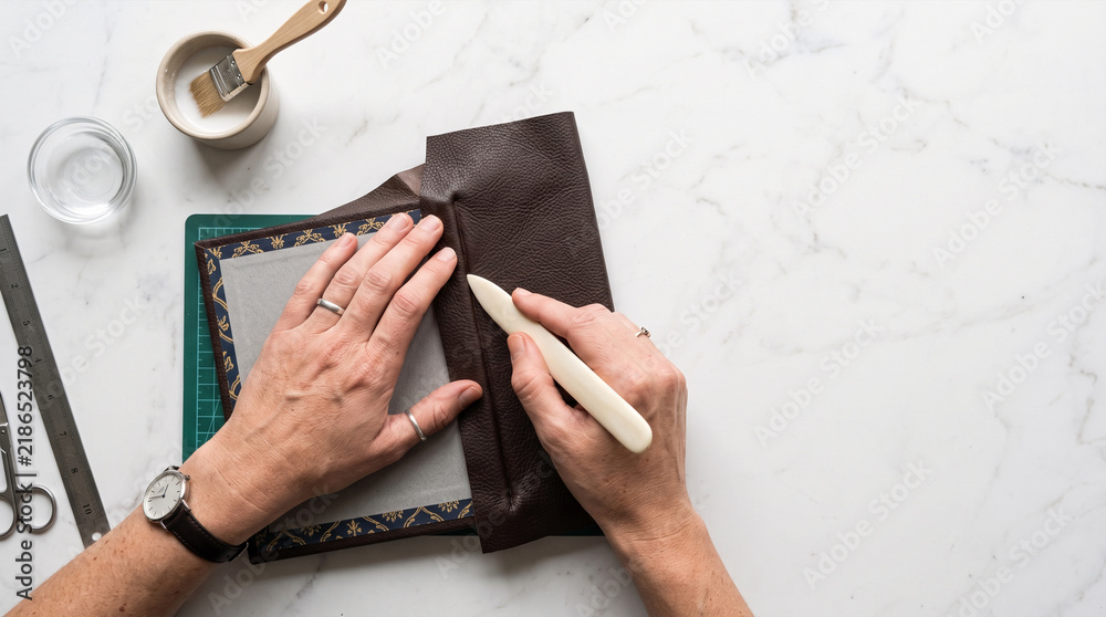 Fototapeta premium Hands crafting a book cover with leather and decorative paper