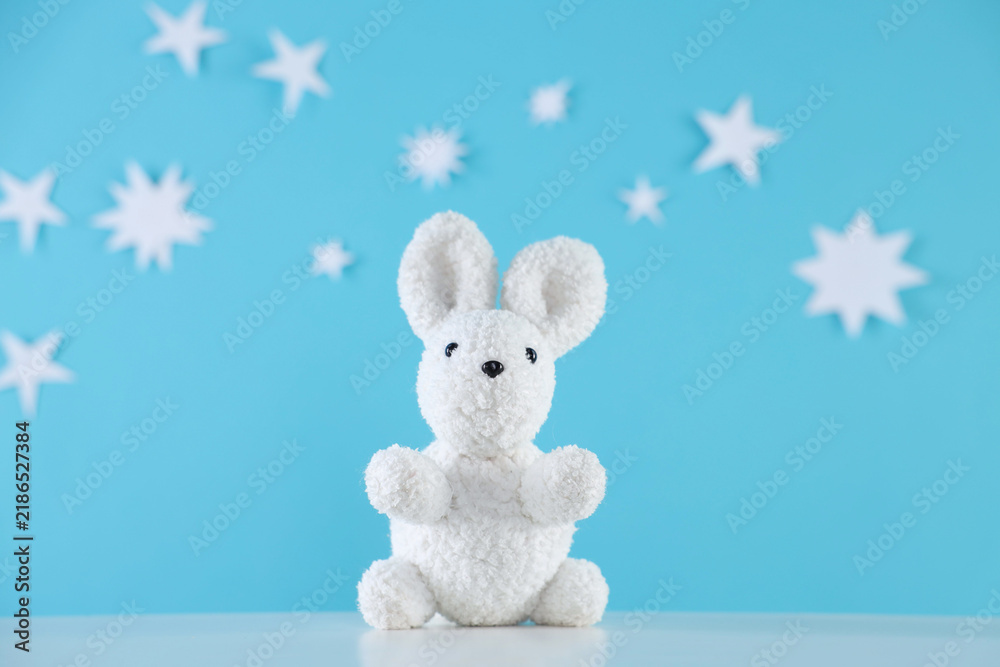 Fototapeta premium One cute toy bunny on white table against light blue background with paper stars