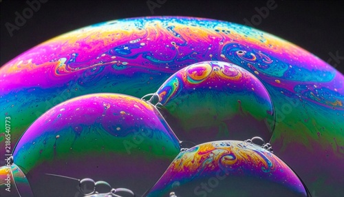 Extreme macro photography displaying colorful iridescent soap bubbles with vibrant rainbow light spectrum patterns on dark background.