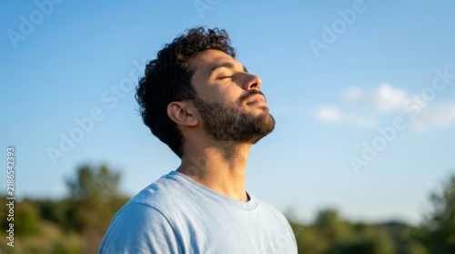 A young man breathes fresh air while tilting his head up in a natural atmosphere.