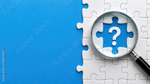 Tapety artystyczne Magnifying glass over a white jigsaw puzzle with a question mark on a blue background representing problem solving