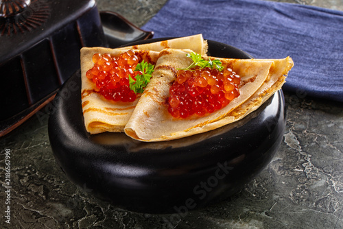 Fotografía Folded crepes topped with vibrant red caviar and fresh parsley on glossy black p