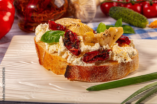 Fotografie Toasted bread slice topped with ricotta cheese, sun dried tomatoes, artichoke he
