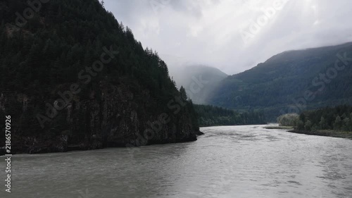 Majestic River Flows Through Lush Forested Mountains Under a Cloudy Sky in British Columbia, Canada