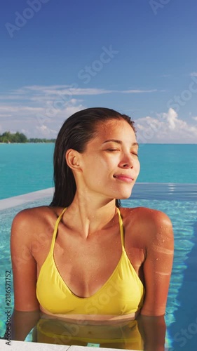Sexy Asian bikini model woman sun tanning in infinity pool at luxury hotel. Swimsuit body summer vacation travel tan. Raw unedited vertical video of real unretouched woman model without any makeup