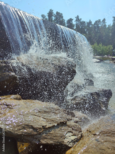 Water cascading over rocks in a forest river under bright sunlight