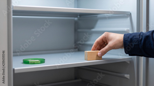 Hand places wooden block on empty refrigerator shelf