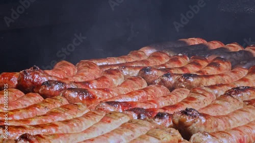 Slow zoom out of sizzling Argentine chorizo sausages grilling on outdoor parilla barbecue