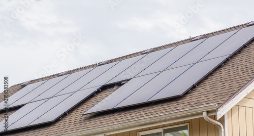 фотографія Modern solar panels installed on a brown shingled roof of a residential house under a bright sky